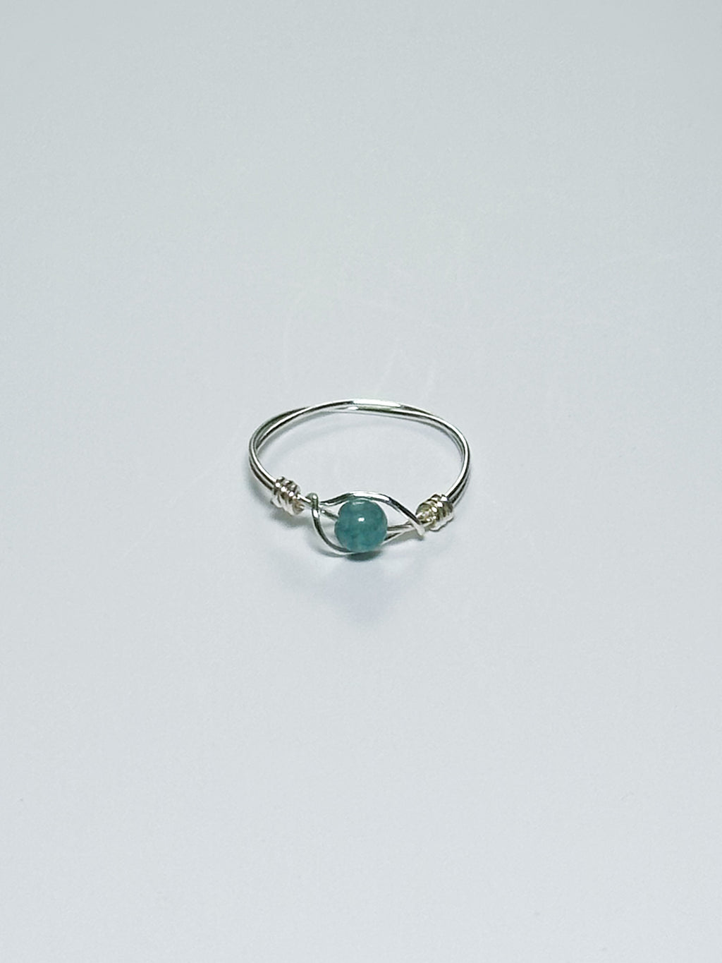 Silver wrapped ring with a green stone on a light gray background