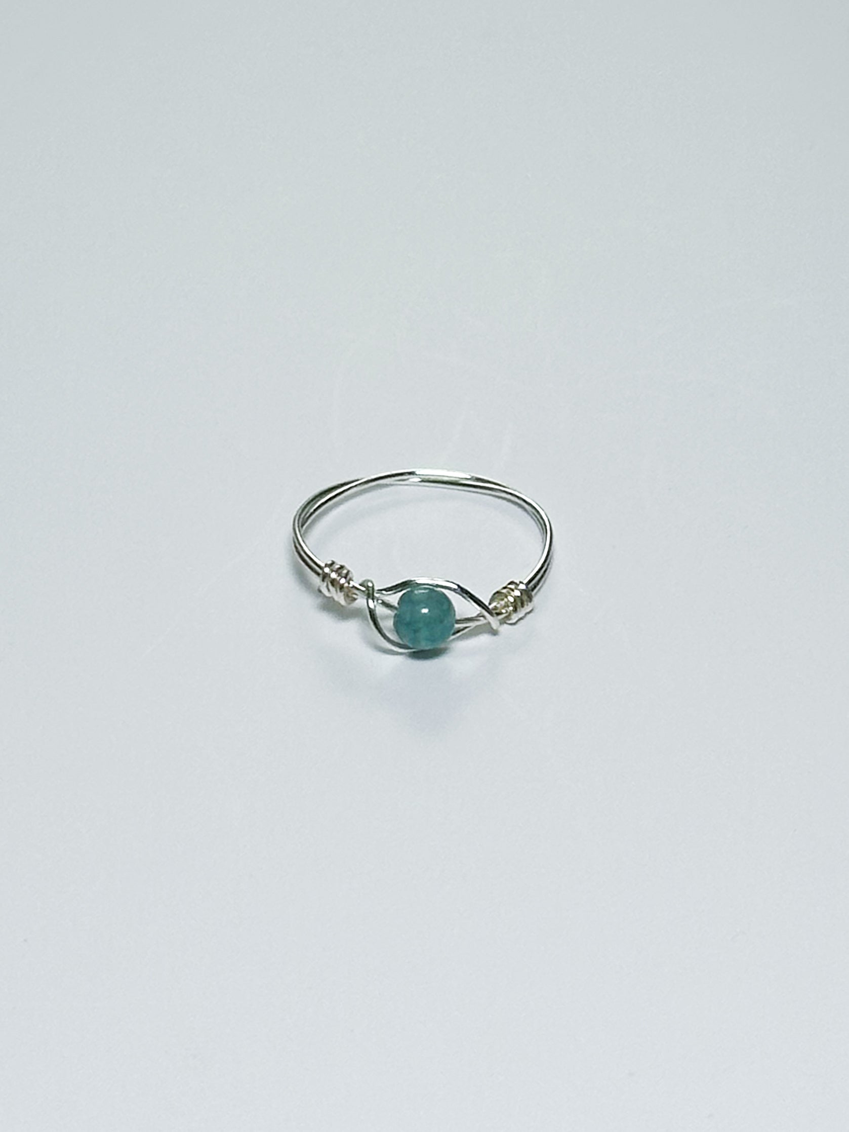 Silver wrapped ring with a green stone on a light gray background