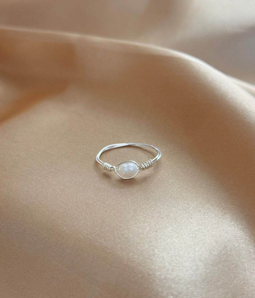 Silver wrapped ring with a pearl on a beige pink fabric background.