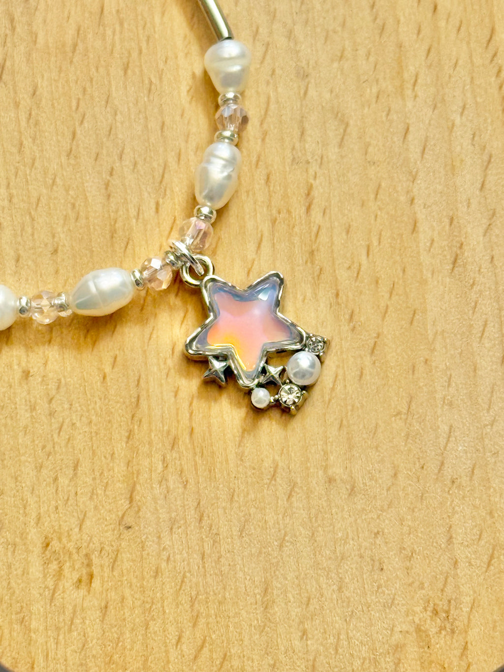 An ultra-close up shot focusing on the star-shaped charm, of a pearl and pink beads bracelet with silver-plated body on a light grey background.