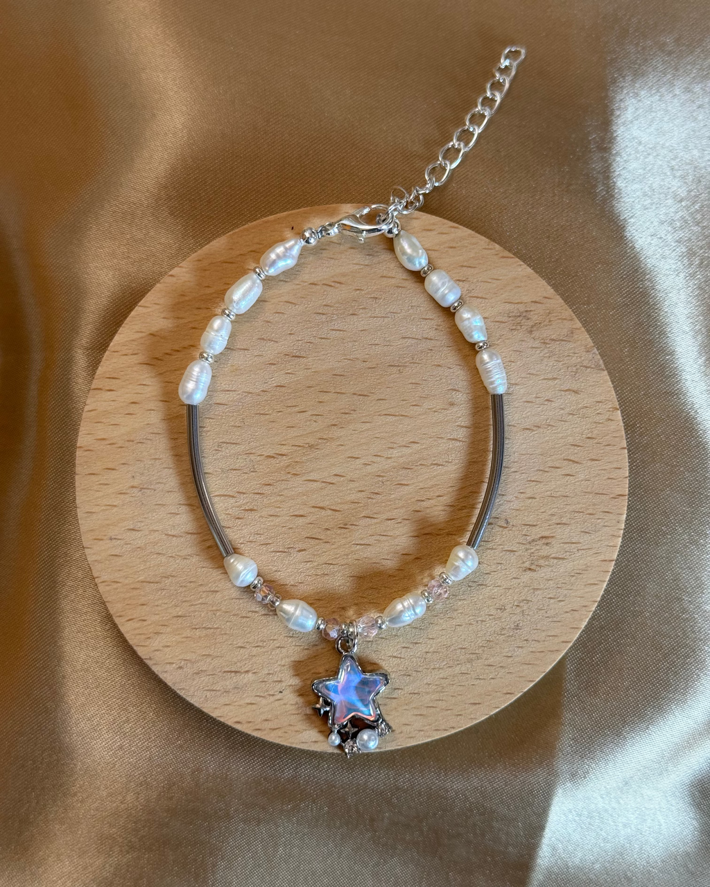 Pearl and pink beads, silver-plated body bracelet with star-shaped charm on a wooden coaster, with beige pink silk background.