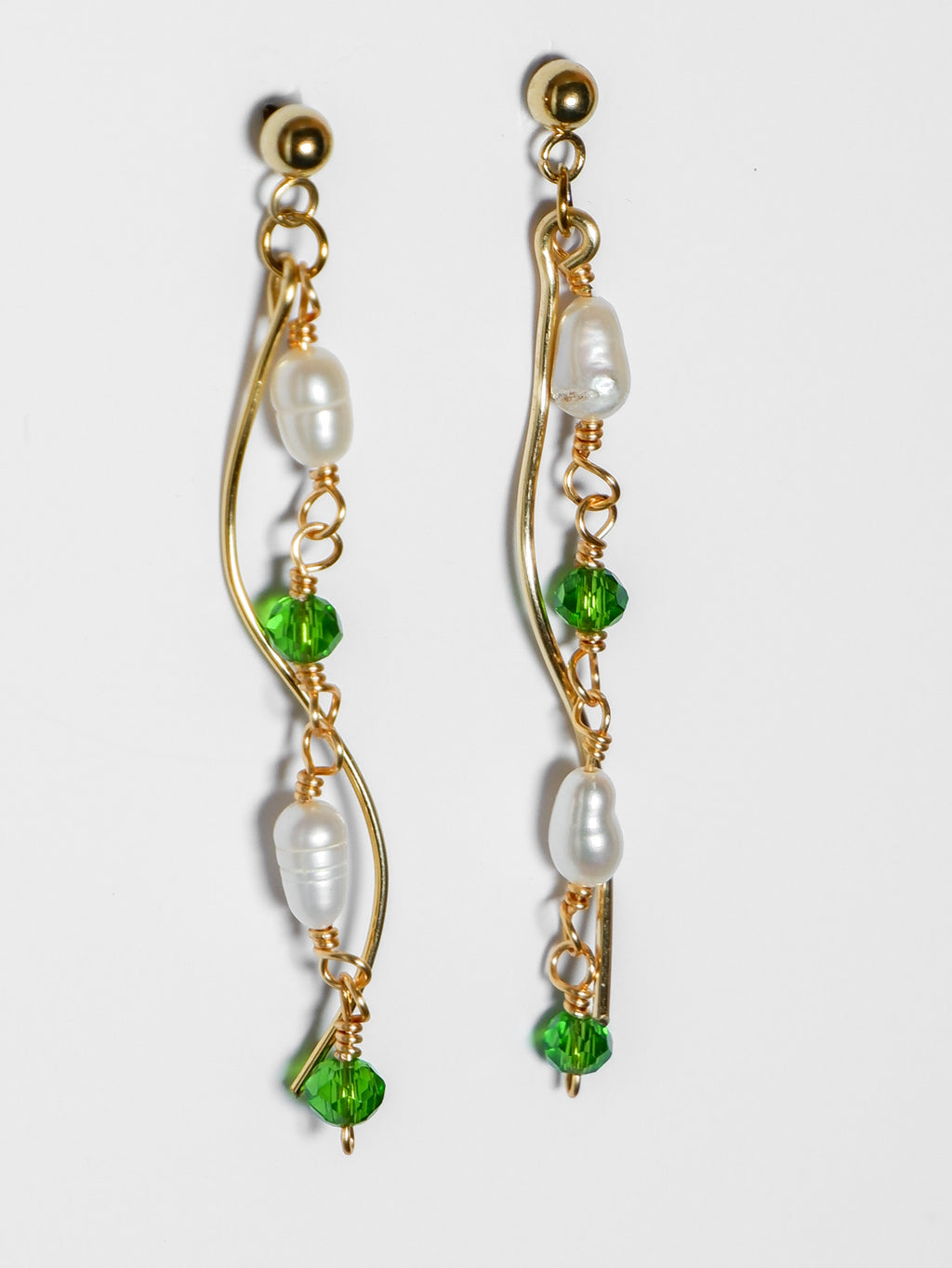 A close-up shot of a Gold pearl earrings with two bodies–one with emerald green beads and pearls linked by hooks, another is a curvy gold-plated body, on a white background.