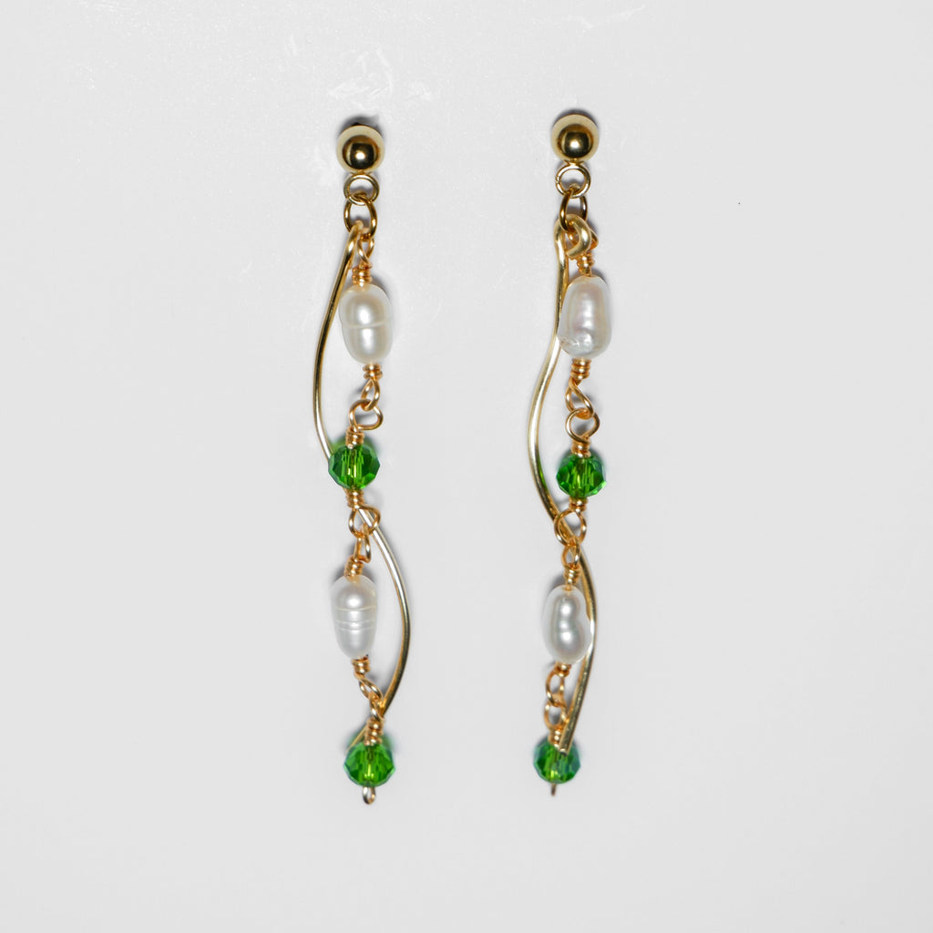 Gold pearl earrings with two bodies–one with emerald green beads and pearls linked by hooks, another is a curvy gold-plated body, on a white background and studio backdrop.