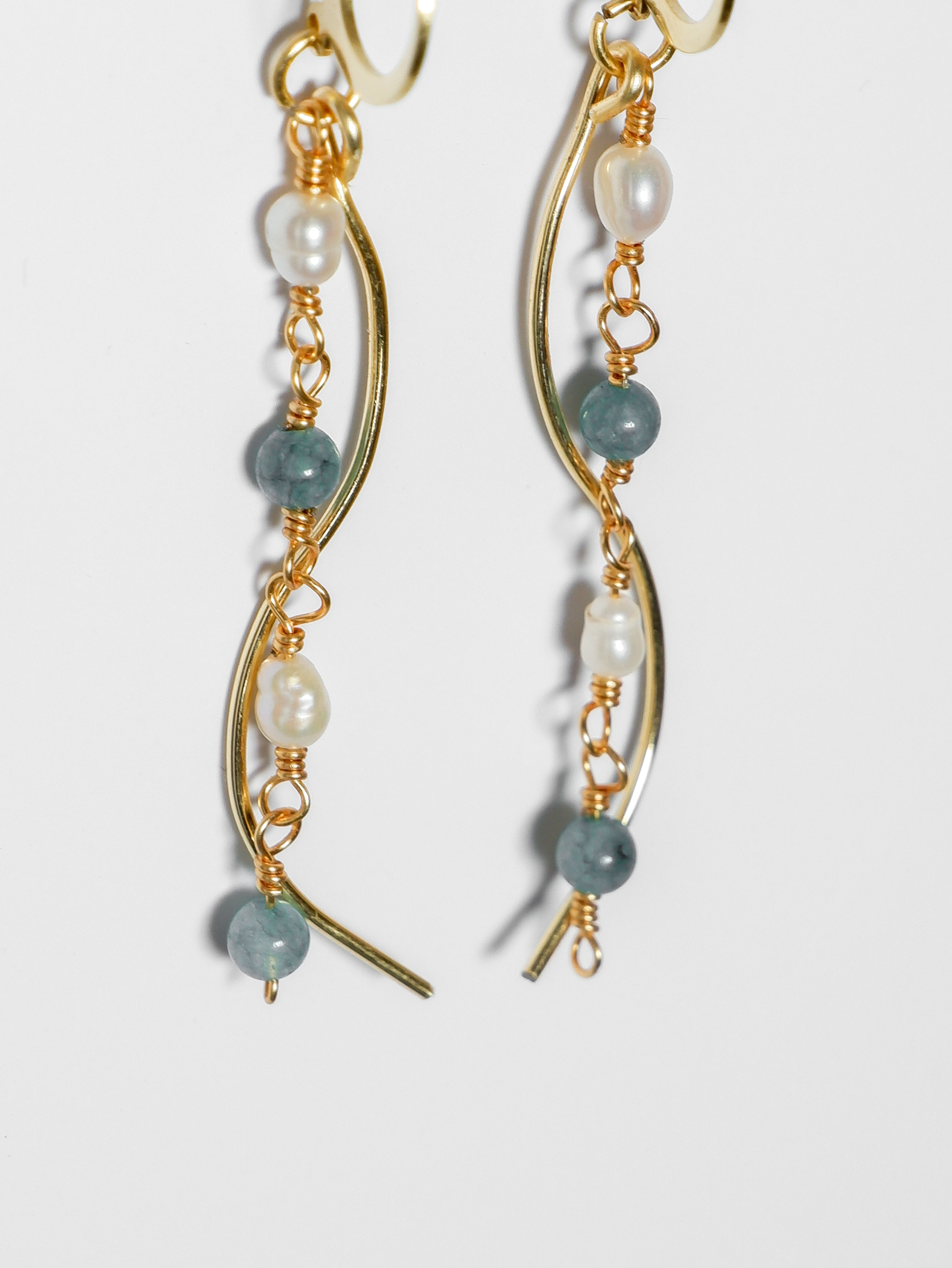 A close-up shot of a Gold pearl earrings with two bodies–one with jade blue stones and pearls linked by hooks, another is a curvy gold-plated body, on a white background.