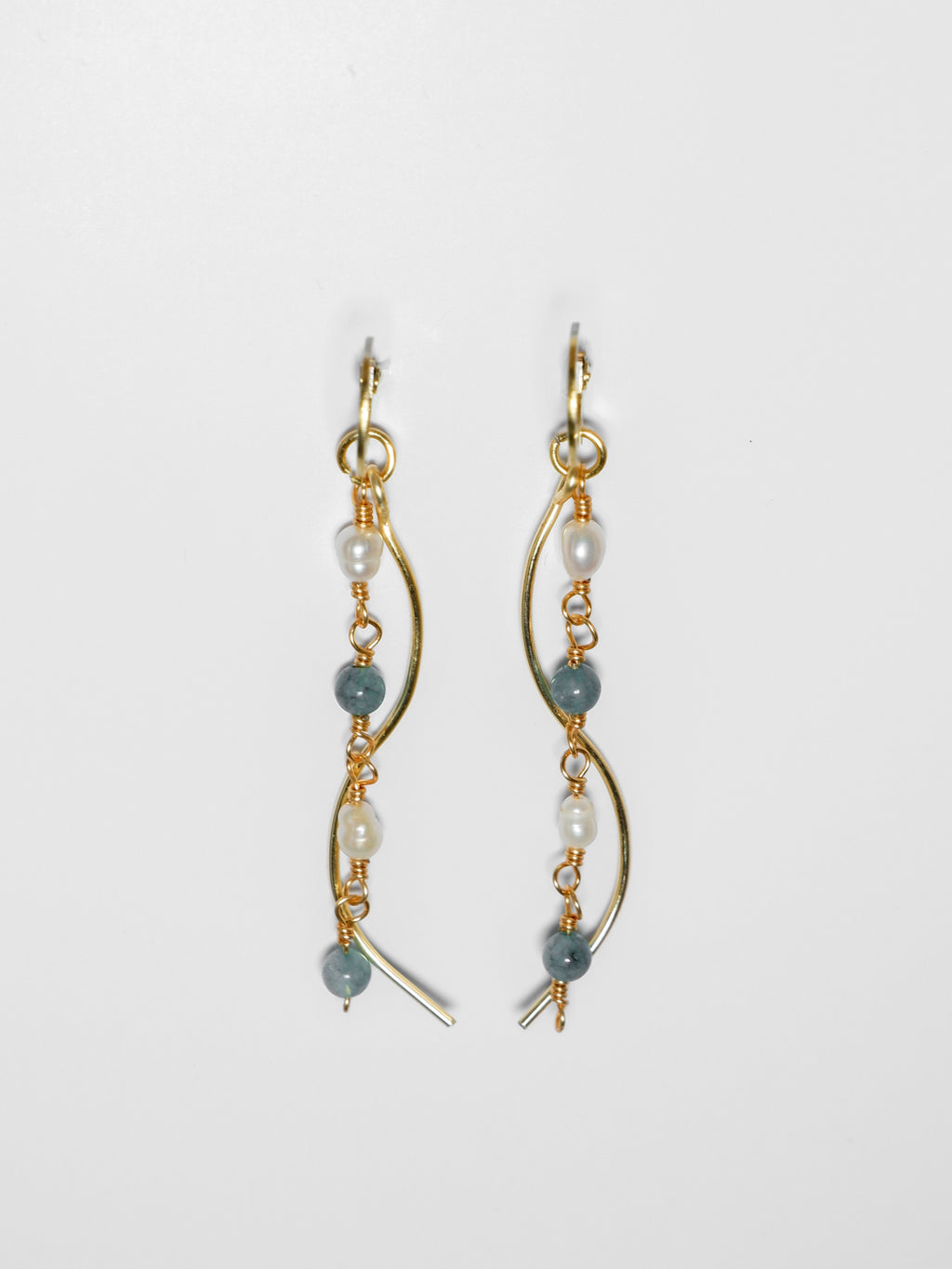 Gold pearl earrings with two bodies–one with jade blue stones and pearls linked by hooks, another is a curvy gold-plated body, on a white background and studio backdrop.