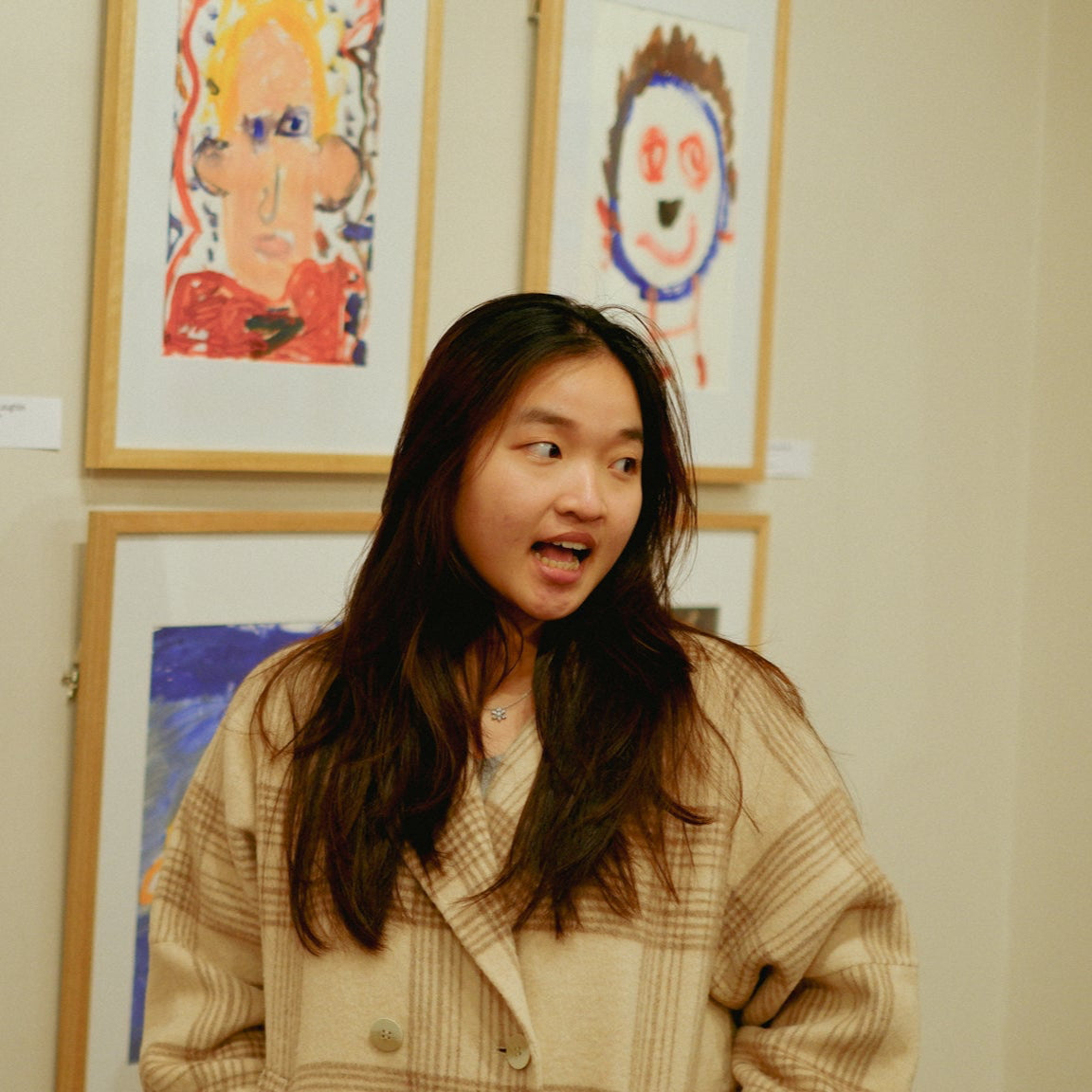 Portrait of the founder Zoey Pham under yellow lights and children's paintings in the background.